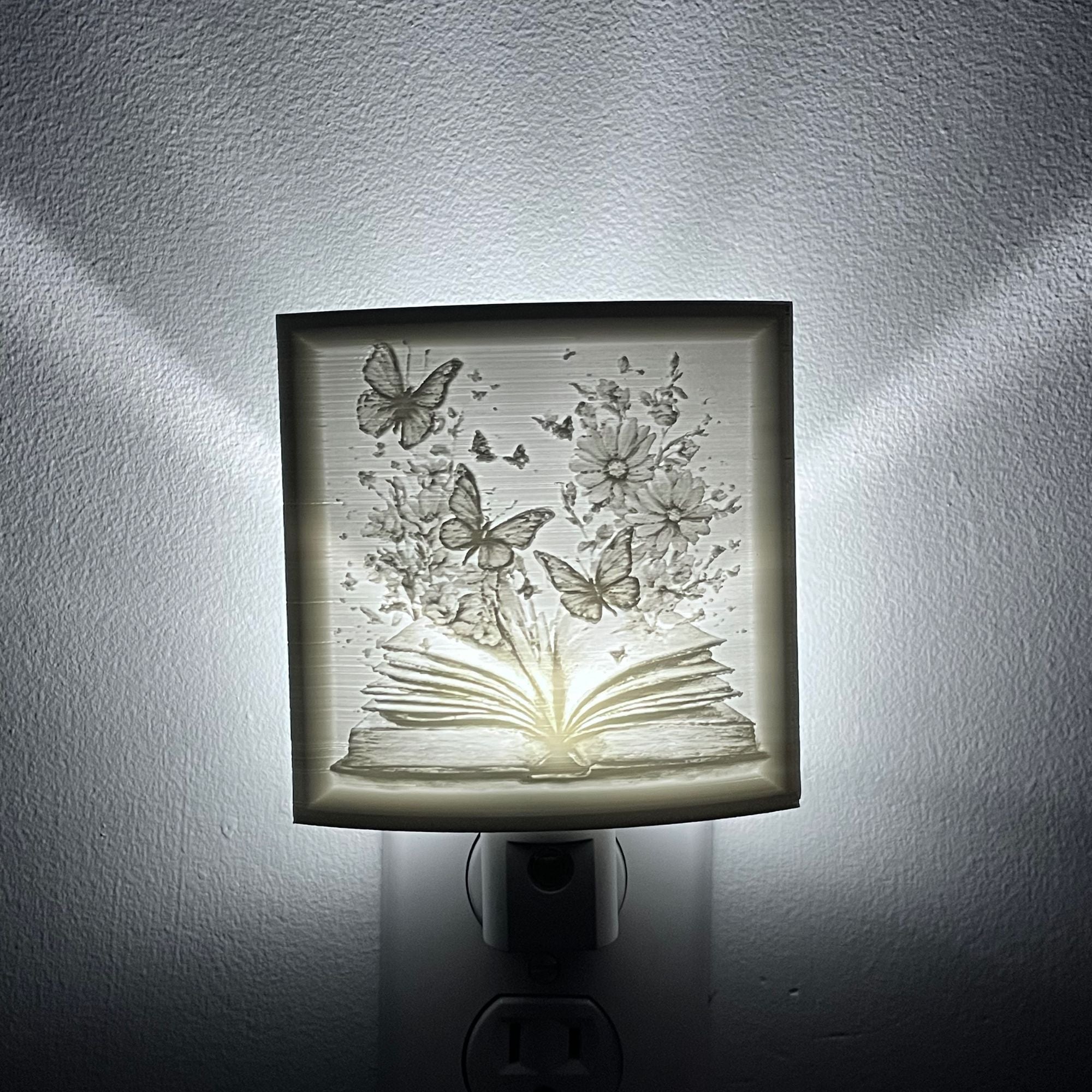 nightlight with a depicting an open book with flowers and butterflies emerging from it.