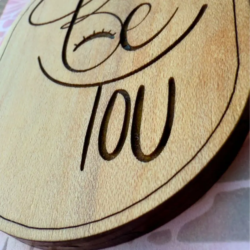 Close up of oval keychain with 'Be You' engraving on a pink background