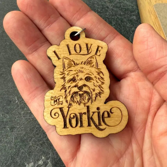 Wooden keychain with 'I love my Yorkie' text held in a hand against a dark background