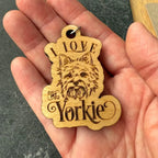 Wooden keychain with 'I love my Yorkie' text held in a hand against a dark background