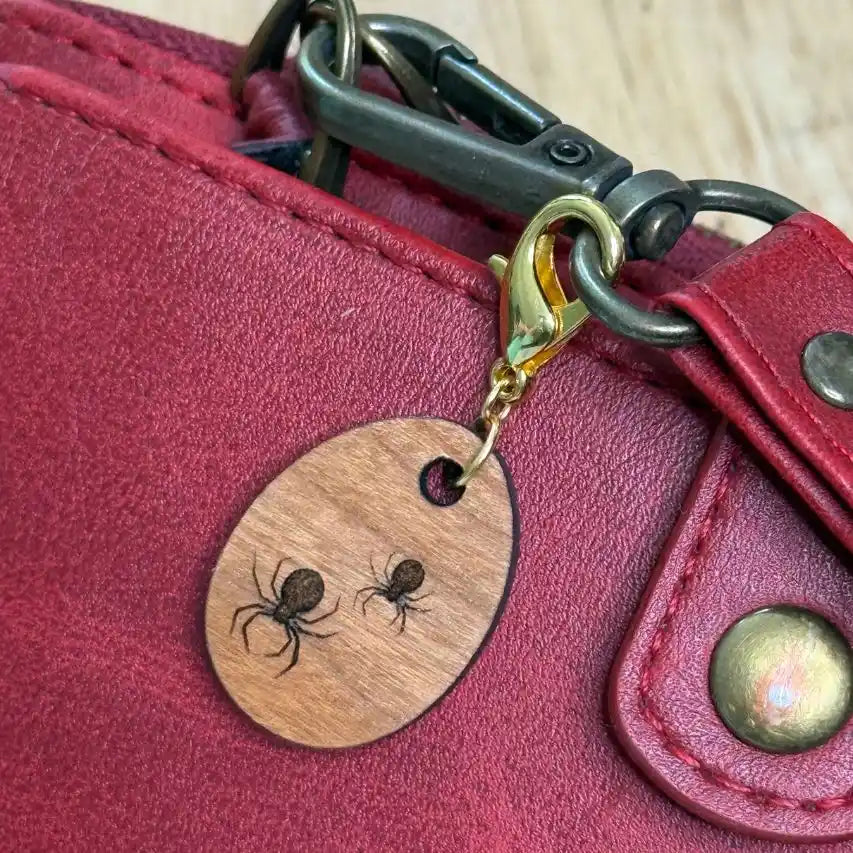 Wooden keychain with spider design attached to a red leather bag.